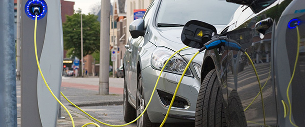 Two electric cars are parked at a parking spot while they are being recharged at a power station